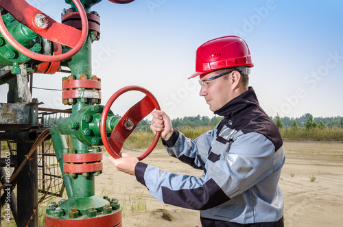 Oilfield worker repairing well head valve wearing red helmet and work clothes with the radio in his pocket. Oil and gas concept. 