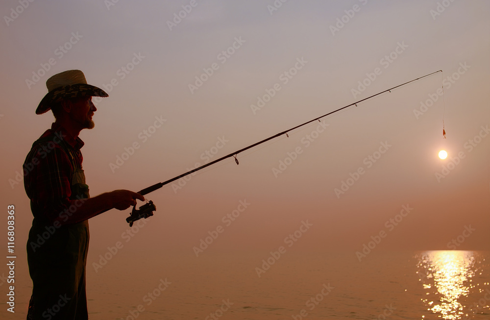 fisherman with a fishing rod on the background of sunset. dark