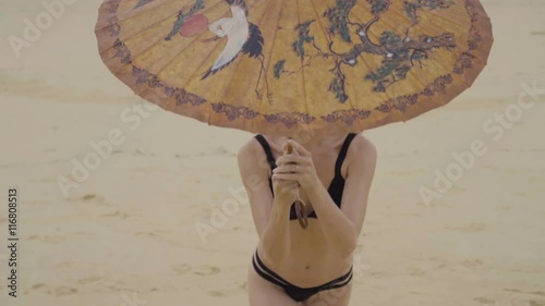 Beautiful blonde glamour woman wearing black swimwear with chinese umbrella smiling and posing on a beautiful summer day at the beach - video in slow motion photo