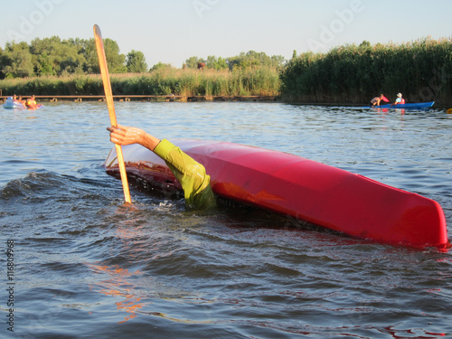 Quadro su tela Man doing eskimo roll with red kayak on the river near the shore