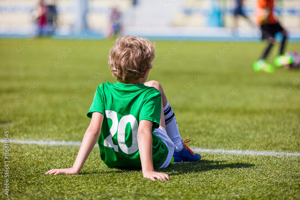 Youth Soccer; Little Soccer Player. Young Boy as a Soccer Player Sitting on Football Field and Watching School Soccer Match