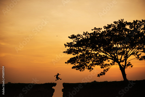 Silhouette of man jumping over cliff on sunset background , business concept