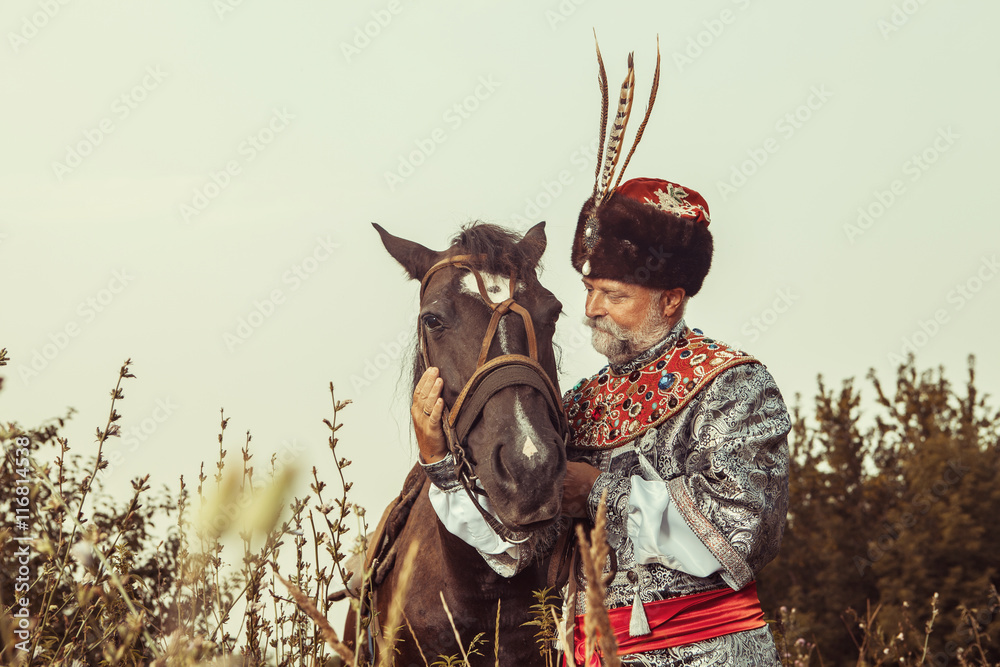 King dressed in medieval costume is stroking his horse 