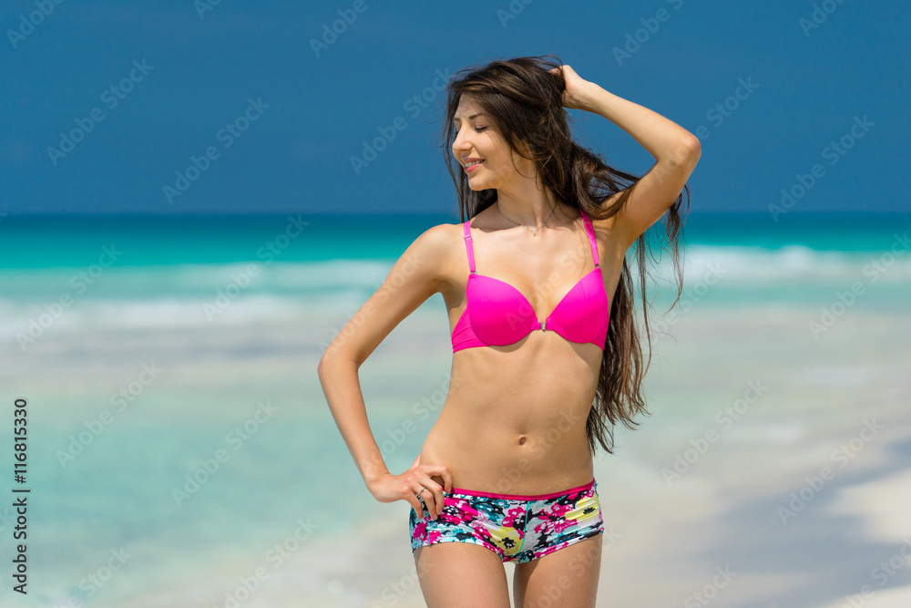 Beautiful young girl in coloured swimsuit is posing on the beach on the background of azure caribbean sea.