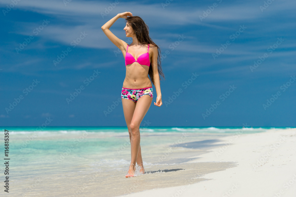 Beautiful young girl in coloured swimsuit is posing on the beach on the background of azure caribbean sea.