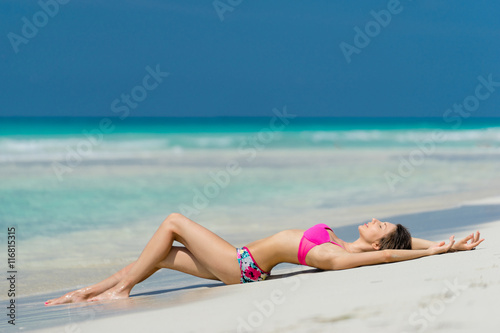 Beautiful young girl in coloured swimsuit is lying on the beach on the background of azure caribbean sea. Hot summer day at the coastline of the Cuba.