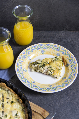 Smoked mackerel and leek tart or quiche. Bottle with juice, gray background, yellow and blue plates.

