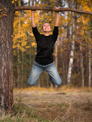 Young woman hanging on a branch with a strained expression on his face on blurred background foliage