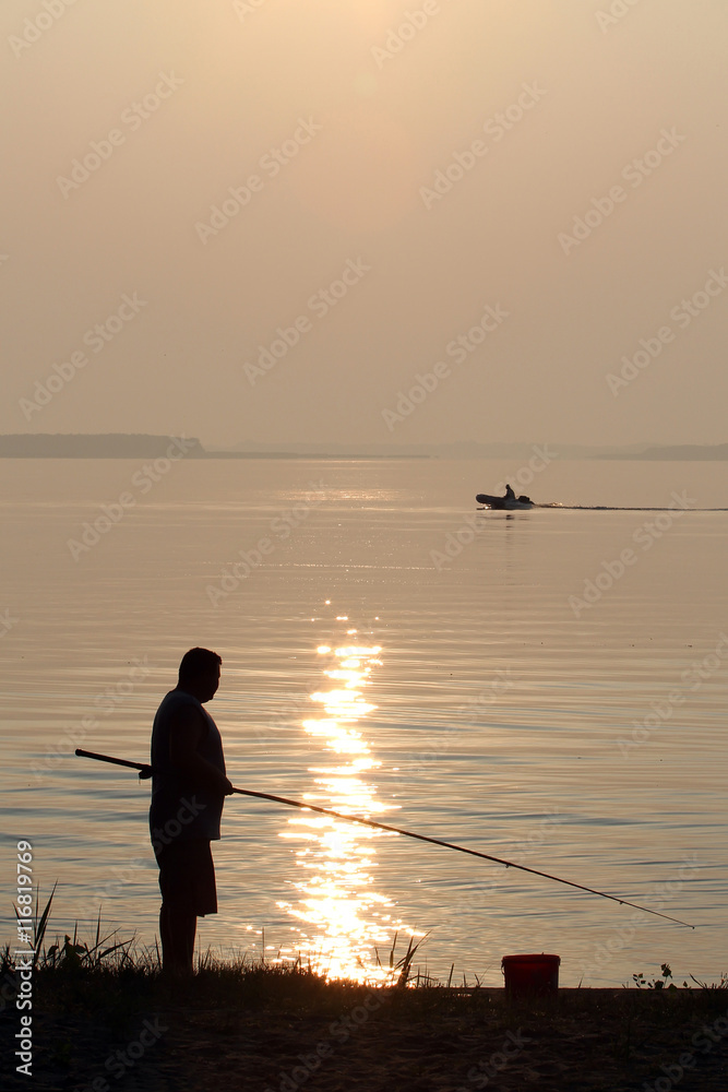 Silhouette of a man with a fishing rod and bucket for fish on th