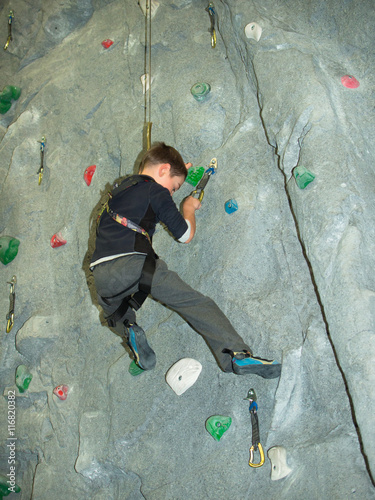 A boy climbs a wall holding on to clip