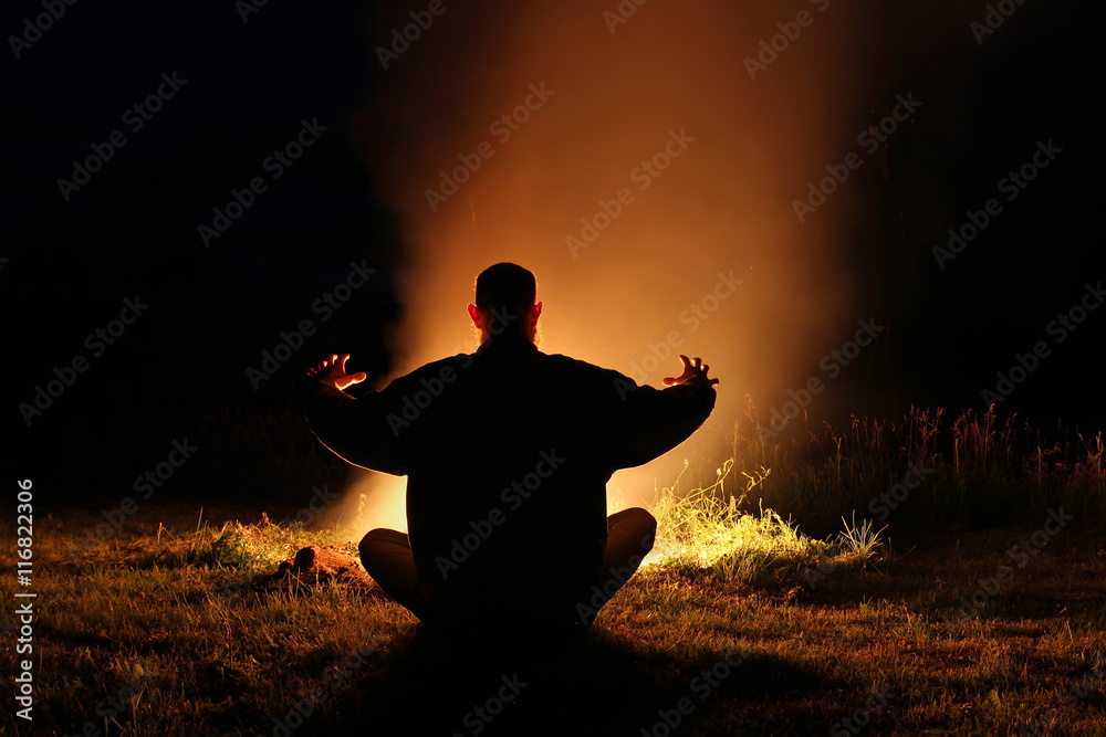 Silhouette of a man sitting in the lotus position at night by th