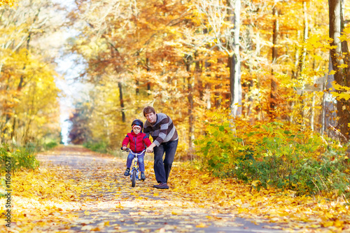 Little kid boy and father with bicycle in autumn forest