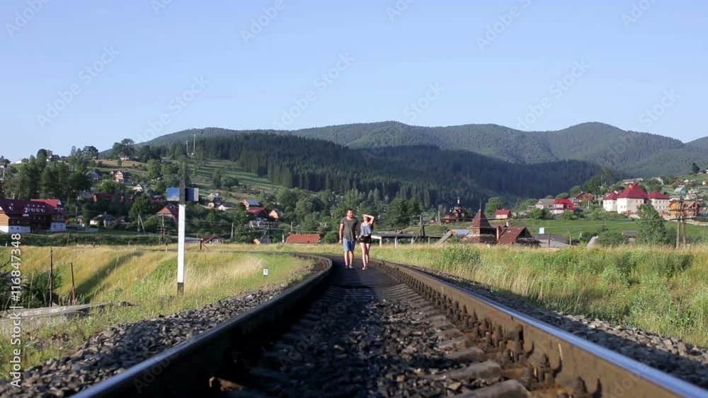 Young couple walking together on railroad in mountains Young couple walking together on railroad in mountains