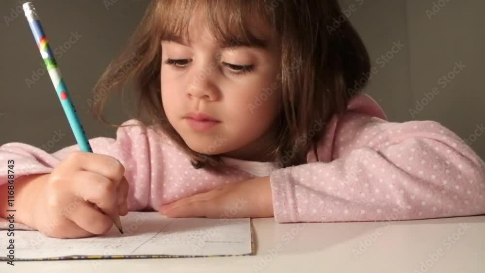 Young girl (age 6-7) writing her homework at the table in her room before bedtime. Real people Education concept Young girl (age 6-7) writing her homework at the table in her room before bedtime. Real people Education concept