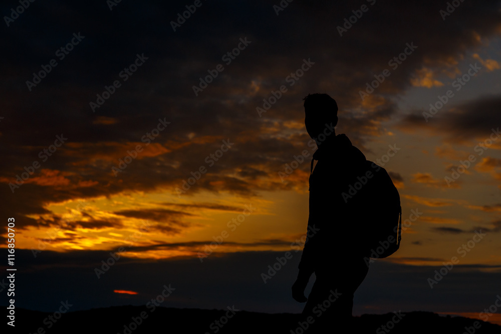 Silhouettes of hiker with backpack enjoying sunset view from top of a mountain