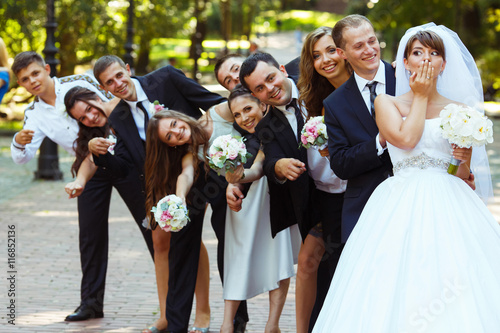 Bride closes her mouth with a palm while groom and friends look