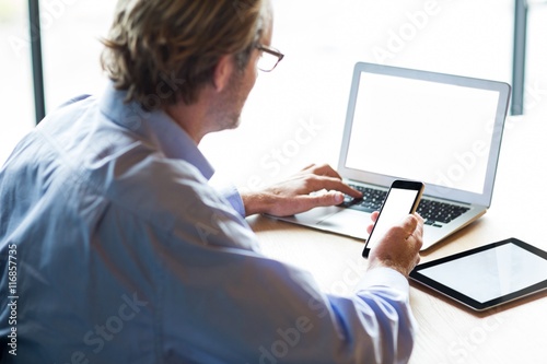 Man using laptop while holding phone in office