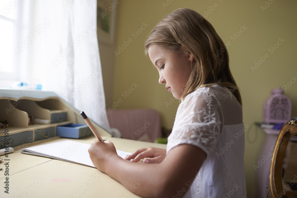 Girl writing in notebook while sitting at desk Girl writing in notebook while sitting at desk
