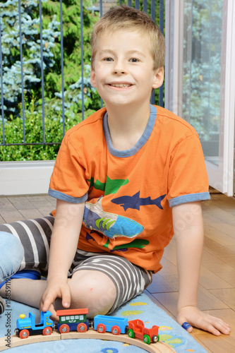 Kleiner Junge spielt mit Holzeisenbahn in Kinderzimmer
