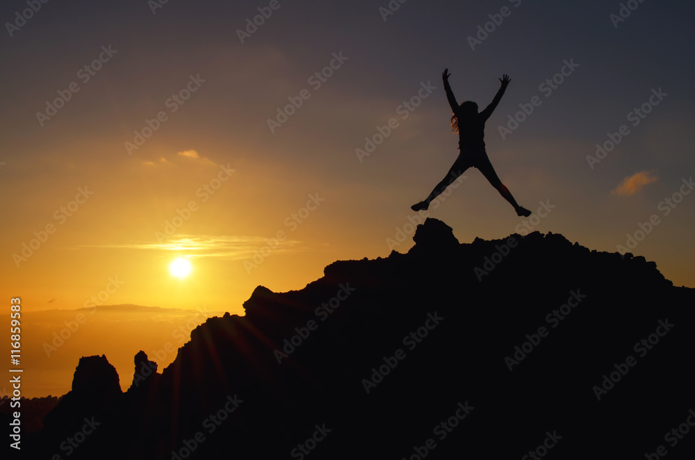 Junge Frau springt bei einem Sonnenuntergang auf einem Berg vor Freude im Urlaub in die Luft