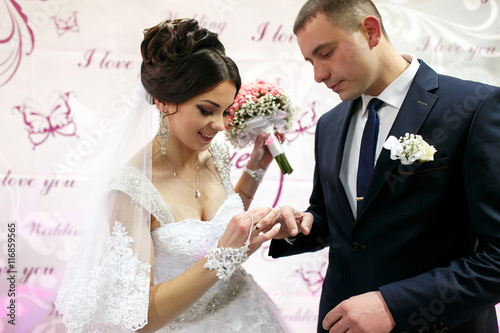 Schilderij op canvas The brides wear rings near wedding banner