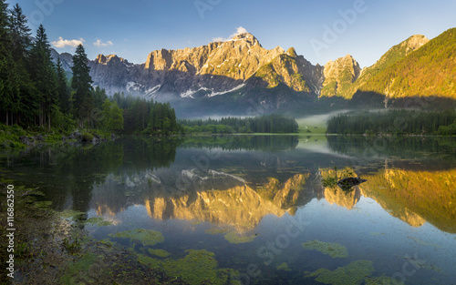 Oświetlone szczyty Alp wschodzącym słońcem nad górskim jeziorem w Alpach Julijskich,Włochy