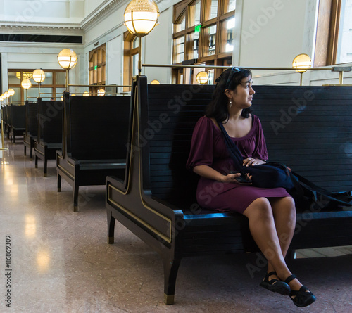 young woman looking out the window for a train in the waiting room  of the renovated historic  Union Station train terminal building 
 photo