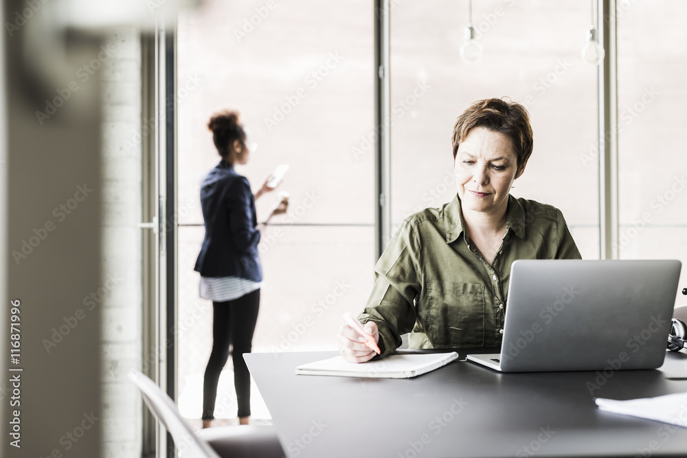 Businesswoman sitting at desk writing down something Businesswoman sitting at desk writing down something