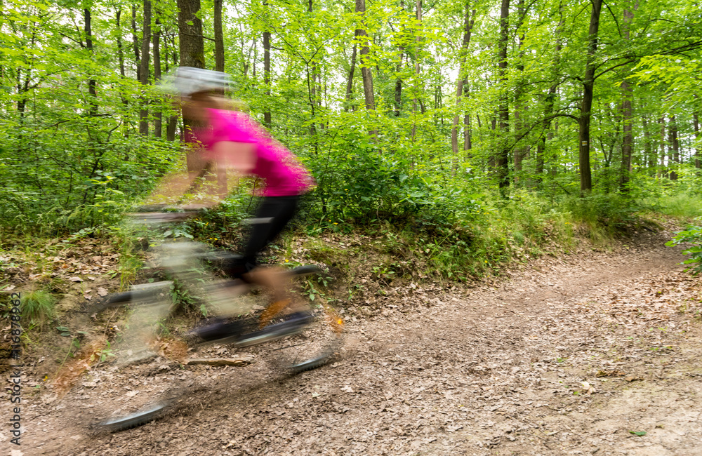 Fototapeta premium Young woman biker in action - motion blur effect on the bike in the forest