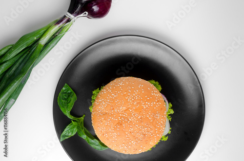 Burger on a black plate on top with a bunch of red onions