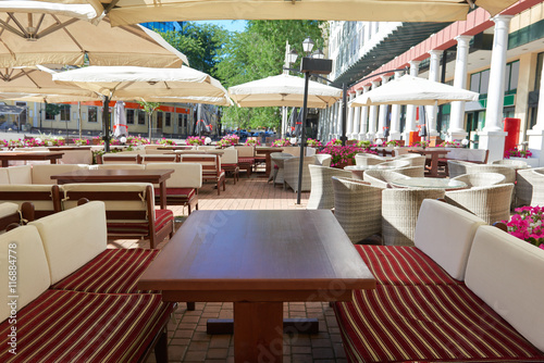 empty street cafe interior in city  tables and chairs under umbrella  summer season  no people