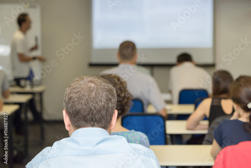 people sitting rear and the teacher near the desk at the business conference