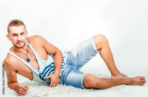 Young athletic man in a vest and jeans shorts on a light background