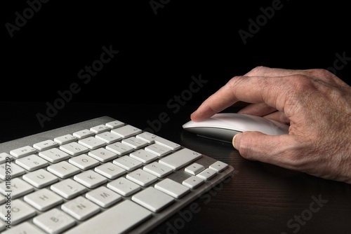Working late on a computer, hand on mouse with section of keyboard isolated on black.