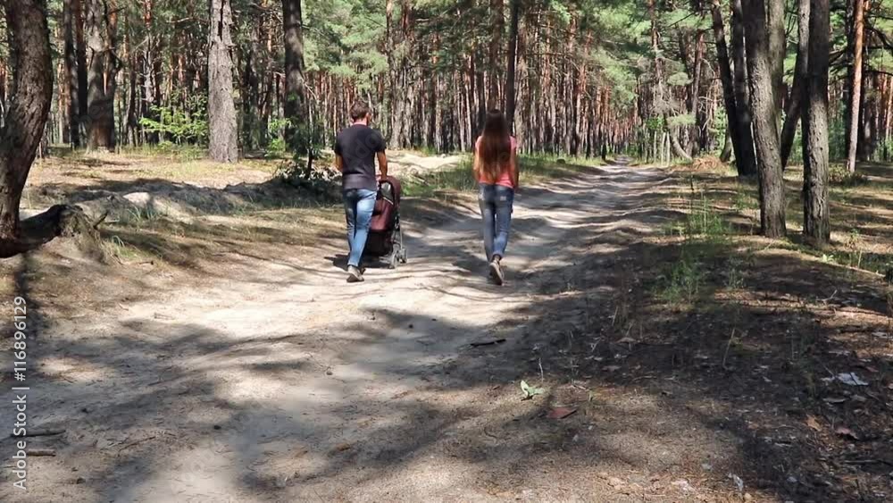 Man carries baby carriage walking through the pine forest along with his wife Man carries baby carriage walking through the pine forest along with his wife