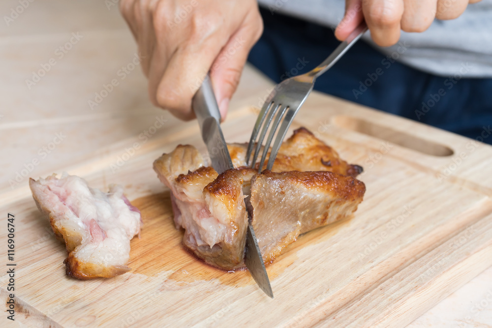 hand with knife cutting medium rare roast pork neck