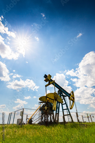 Oil field with old pump jack, profiled on blue sky with white clouds, on a bright day