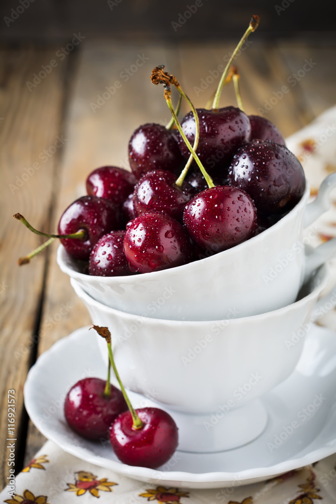 Fresh cherry berries in a white cup on a dark wooden background.Selective focus. Fresh cherry berries in a white cup on a dark wooden background.Selective focus.
