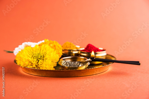 Beautifully Decorated Pooja Thali for diwali celebration to worship, huldi or turmeric powder and kumkum, flowers, scented sticks in brass plate on orange background, hindu puja thali photo