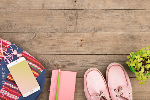 colorful bag, smart phone, headphones, notepad and pink shoes on wooden desk