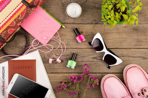 straw bag, smart phone, headphones, sunglasses, notepad, pink shoes, passport and book on wooden desk
