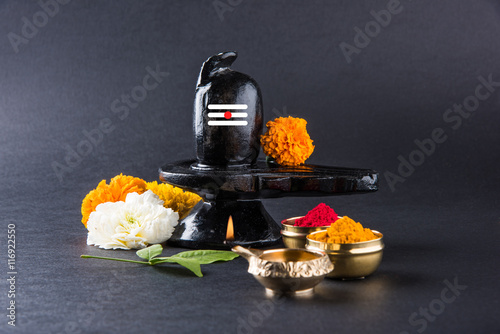 Shiva Linga made up of black stone decorated with flowers & bael leaf known as Aegle marmelos, over black background, maha shiva ratri a festival of hindu God shankar or shankar bhagwan or bholenath