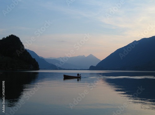 Dusk shot of lone fishing boat on Brienzersee lake, Switzerland with Niesen mountain in far distance photo