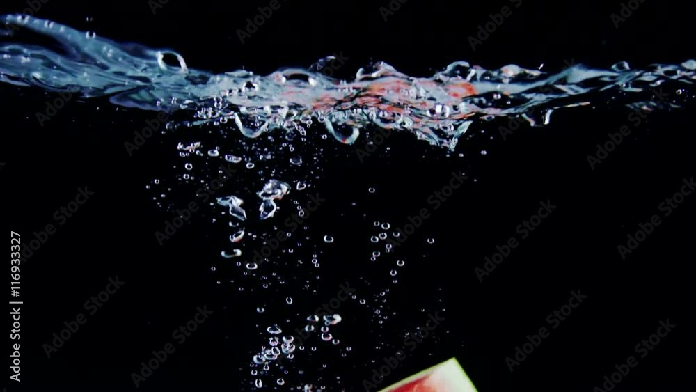 Fresh ripe watermelon slice falls into water with splashes on black background