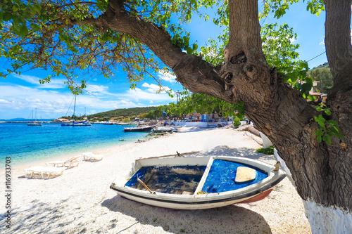 Sunny summer beach in Greece with sun beds and small boat photo
