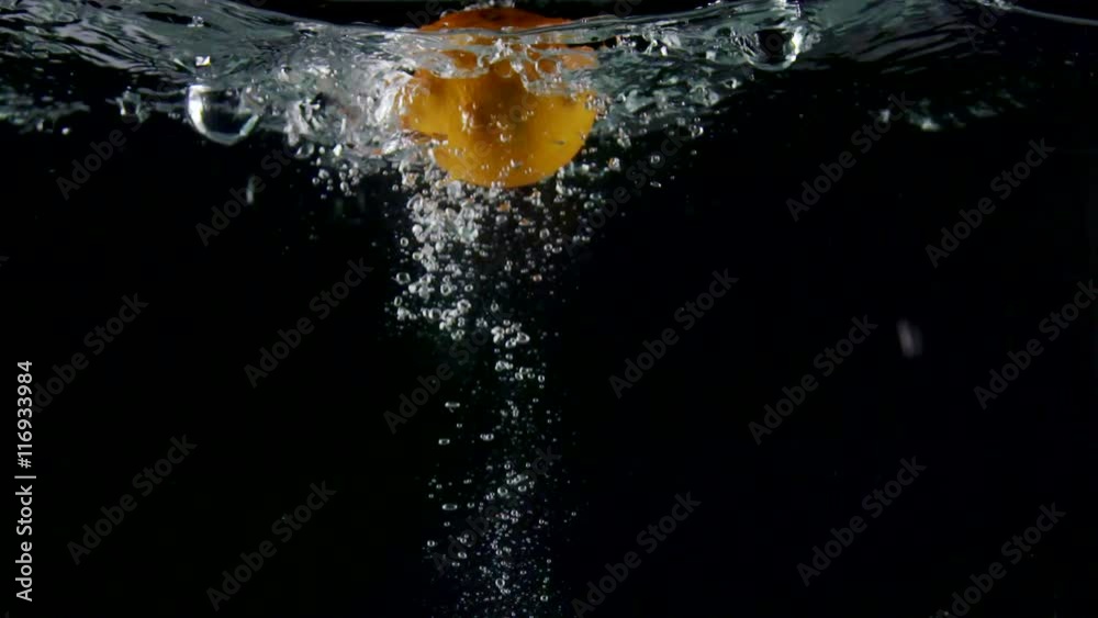 Fresh fruit orange falling into water with splash on black background close-up slow motion