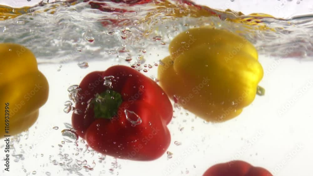 Slow motion of fresh vegetables sweet yellow red bell peppers falling into clear water with splashes on white background