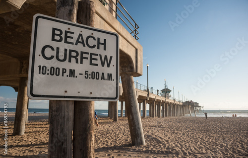 Beach curfew times on sign under the pier of Huntington beach in Southern California photo