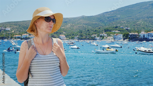 A tourist in a hat and sunglasses, walking along the promenade. Against the backdrop of the bay with yachts and boats, remove visible mountains.