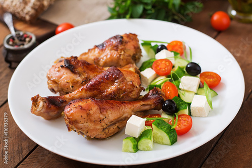 Appetizing oven baked golden chicken drumsticks and Greek salad